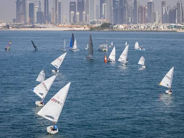A fleet of dinghies racing in front of the Dubai skyline, a club photograph.